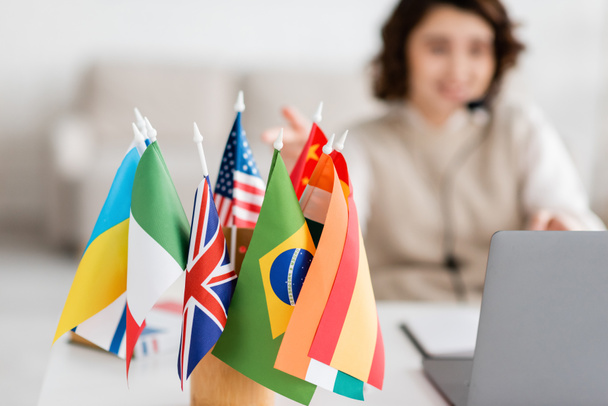 selektywne skupienie się na różnych flagach międzynarodowych w pobliżu niewyraźnego laptopa i nauczyciela języka o lekcji online w domu - Zdjęcie, obraz