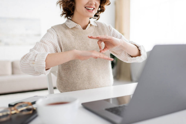 καλλιεργημένη άποψη του χαρούμενου δασκάλου που δείχνει χειρονομία νοηματικής γλώσσας κατά τη διάρκεια online μαθήματος στο laptop  - Φωτογραφία, εικόνα