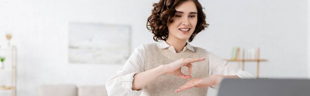счастливый учитель с кудрявыми волосами, показывающий жест языка жестов во время онлайн-урока на ноутбуке, баннер  - Фото, изображение