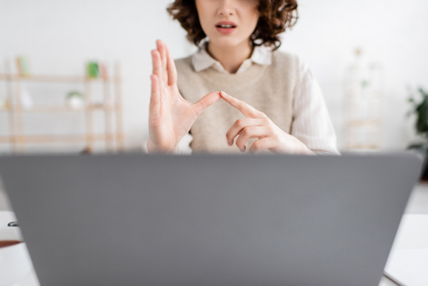 обрезанный вид женщины преподавания языка жестов алфавит рядом с размытым ноутбуком дома - Фото, изображение