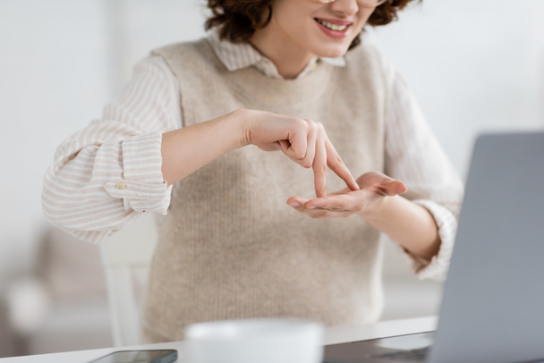 обрезанный вид улыбающейся женщины, показывающей слово стоять во время преподавания языка жестов во время онлайн-урока на ноутбуке  - Фото, изображение