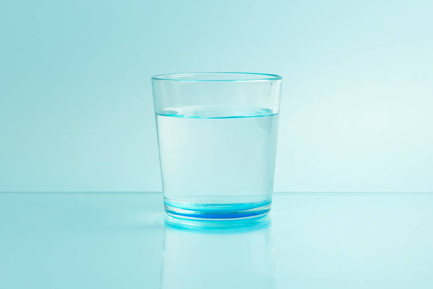 Glas met zuiver helder smeltwater op een blauwe ondergrond - Foto, afbeelding