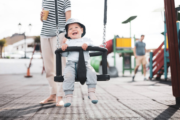 Mother pushing her infant baby boy child on a swing on playground outdoors - Fotoğraf, Görsel