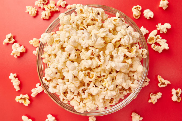 A bowl on a red background is completely filled with popcorn. - Фото, изображение