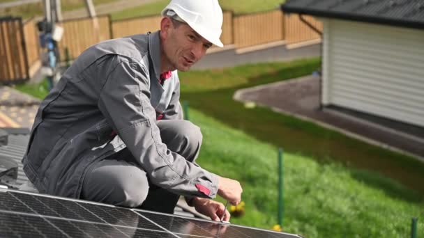 Man technician mounting photovoltaic solar panels on roof of house. Engineer in helmet installing solar module system with help of hex key. Concept of alternative, renewable energy. - Footage, Video