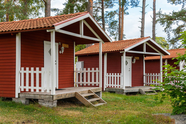 Małe czerwone drewniane domki w skandynawskim stylu szwedzkim w pobliżu pola golfowego. Klasyczne, przytulne mieszkanie. Idealne miejsce dla introwertyków.  - Zdjęcie, obraz