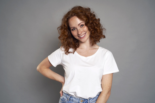 Portrait of red head caucasian woman wearing blue jeans and white tshirt on grey background - Photo, Image