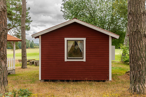 Winzige kleine rote Holzhäuser im skandinavisch-schwedischen Stil in der Nähe eines Golfplatzes. Vintage, gemütliches Gehäuse. Idealer Ort für Introvertierte.  - Foto, Bild