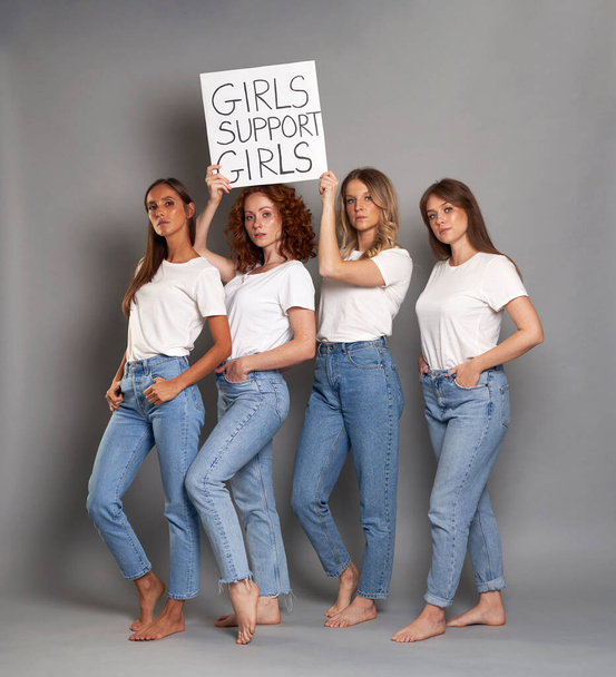Four young caucasian women wearing white tshirt and holding banner above heads - Фото, изображение