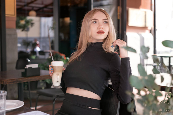 Rozmyślanie atrakcyjna młoda blondynka siedzi przy stole w kawiarni z filiżanką kawy cappuccino latte - Zdjęcie, obraz