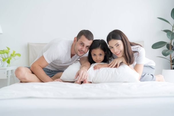 Piękne rodzice i córka szczęśliwy uśmiechnięte twarze lounging w wygodnym białym łóżku. - Zdjęcie, obraz
