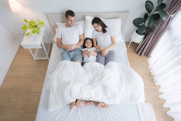 Los padres encantadores y la hija feliz sonriendo caras descansando en una cómoda cama blanca. - Foto, imagen