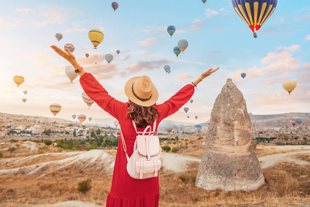 En un día de verano en Capadocia, Turquía, la chica en su bonito vestido se encuentra hipnotizada por la elegante vista de globos de aire en el cielo. - Foto, Imagen