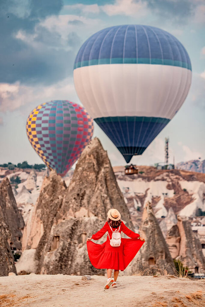 Geïsoleerd door de zwevende luchtballonnen, bleef het meisje stil als in een trance, haar jurk een levendige rode tegen de oranje zandsteen van Cappadocië. - Foto, afbeelding