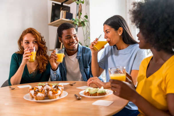 Multiethnic friends having fun at a breakfast with orange juice and muffins at home - Photo, Image