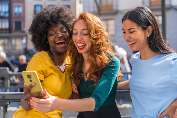 Three multiracial young women on the street taking a selfie in the city, outdoors, friendship, feminist and technology concept - Fotografie, Obrázek
