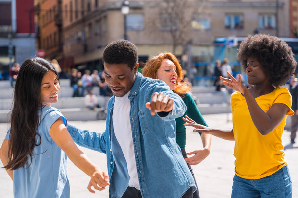 Amigos jóvenes multiétnicos bailando en una plaza de la ciudad, grupo auténtico de amigos diversos divirtiéndose - Foto, imagen