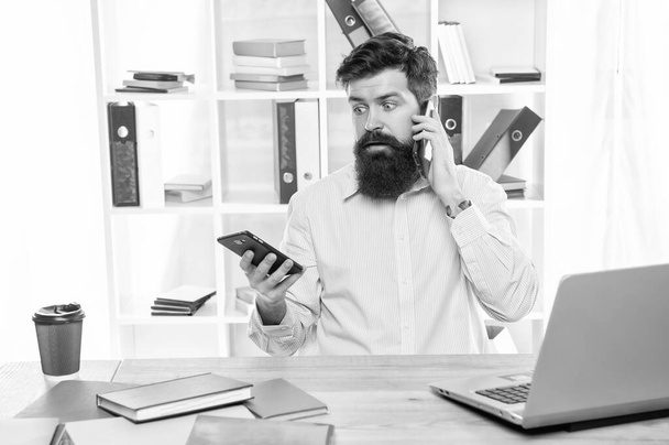 Shocked businessman talking on cellphone using smartphone at office desk, mobility. - Foto, Imagen