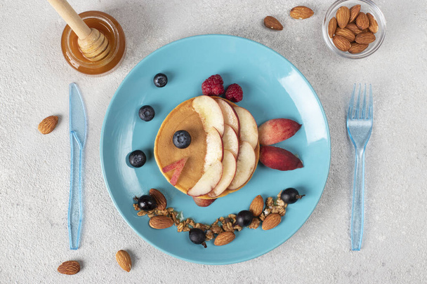 Panqueque en forma de pescado con melocotones, bayas, granola y almendras en un plato azul, idea de desayuno para niños, vista superior - Foto, Imagen