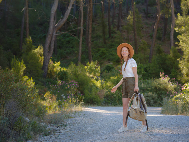 Кавказская рыжая молодая красивая женщина-турист путешествует одна в лесу. Привлекательный путешественник осмотреться и исследовать во время прогулки в лесу природы со счастьем и весельем во время отпуска поездки. - Фото, изображение