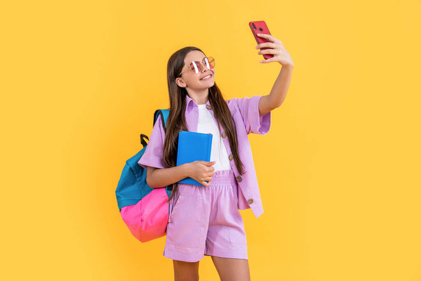 Selfie Teenager Schulmädchen im Studio. Selfie Teenager Schulmädchen im Hintergrund. Foto von Selfie Teenager Schulmädchen mit Handy. Selfie Teen Schulmädchen isoliert auf gelb. - Foto, Bild