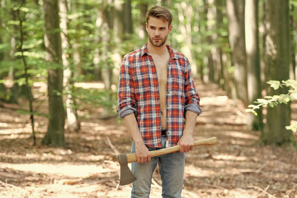 Unshaven man in lumberjack style standing with axe forest background. - Zdjęcie, obraz