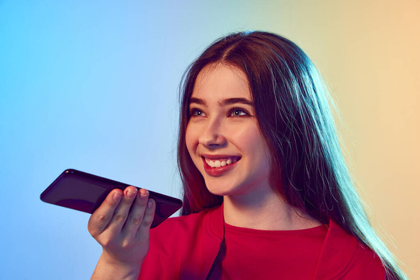 Smiling, enthusiastic. Nice-looking teen girl using cell phone over gradient blue-yellow background. Concept of communiction, friendship, sales, remoute work, technology. - Photo, Image