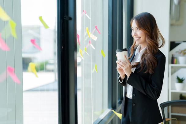 Empresária asiática feliz em um terno segurando uma xícara de café Bebida refrescante no escritório. - Foto, Imagem