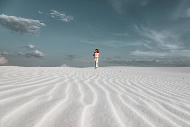 Retrato de una hermosa mujer rubia embarazada con un vestido blanco sobre un fondo desierto. Arena ligera, accesorios de moda con estilo, tatuaje flash, viento y sol de verano. Felicidad de la maternidad, expectativa - Foto, Imagen