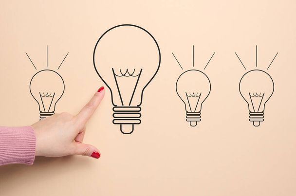 Eine gezeichnete Glühbirne und eine darauf zeigende weibliche Hand, Konzept der Suche nach neuen Ideen, Innovation - Foto, Bild