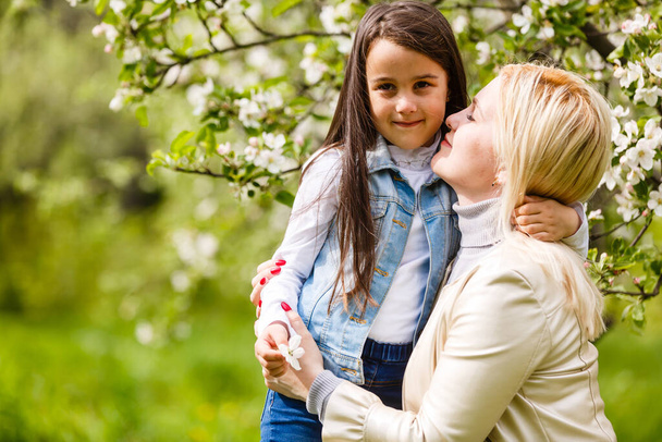 Klein meisje met haar moeder in bloeiende appelboomgaard op zonnige lentedag - Foto, afbeelding