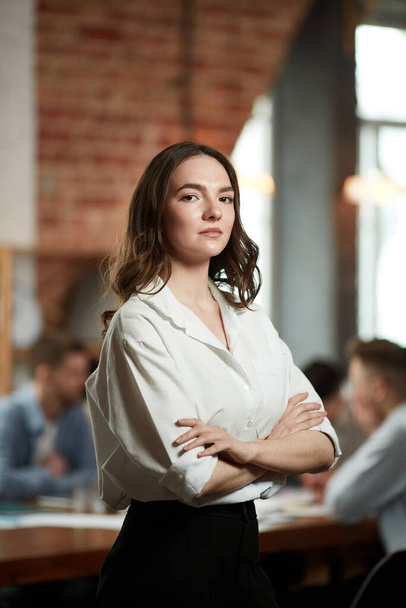 Team leader. Serious ambitious young woman in formal wear attentively looking at camera. Blurred employees on background in office. Concept of business, teamwork, career development, brainstorming - Фото, зображення