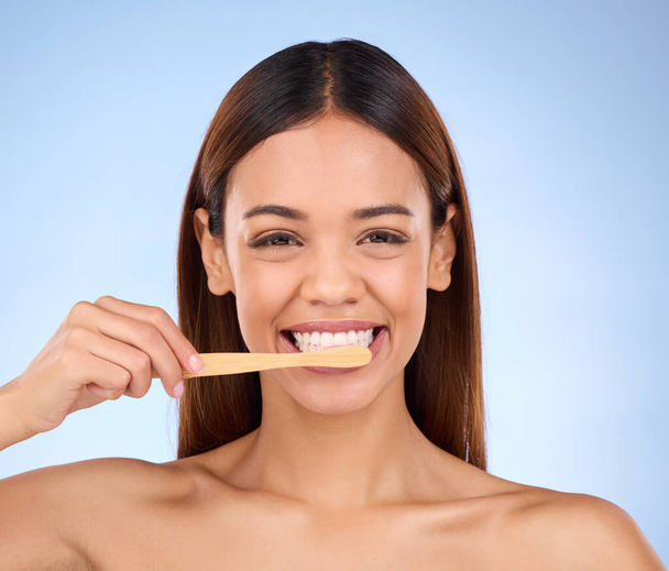 Portret, tandenborstel en glimlach met een modelvrouw in de studio op een blauwe achtergrond voor mondhygiëne. Mond, reiniging en tandheelkundige met een aantrekkelijke jonge vrouw poetsen haar tanden voor whitening. - Foto, afbeelding