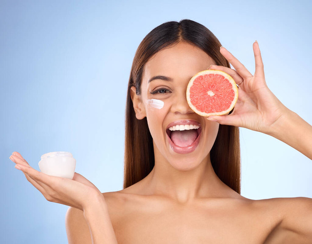 Woman, moisturizer cream and grapefruit for natural skincare beauty and vitamin C against blue studio background. Portrait of happy female holding fruit, creme or lotion for healthy organic products. - Фото, зображення