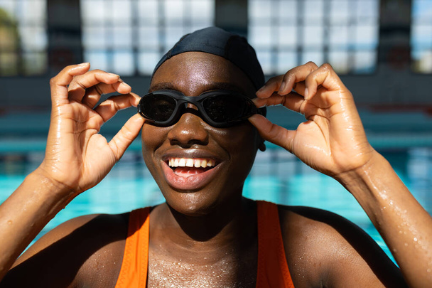 Jeune femme noire souriante tout en ajustant ses lunettes de bain à la piscine chauffée - Photo, image