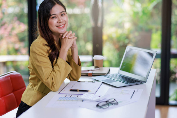 Concept of business office woman working,Businesswoman smile while working about her invesment plan with analyzing document and business investment graph data by using laptop on desk in workstation. - Foto, imagen