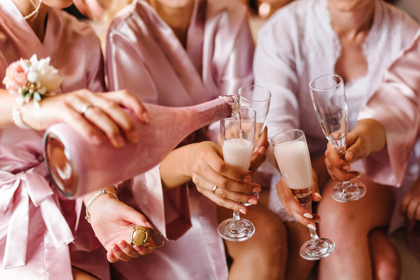 Young bridesmaids clinking with glasses of champagne in hotel room. Closeup photo of cheerful girls celebrating a bachelorette party. Females have toast with wine. - Foto, imagen