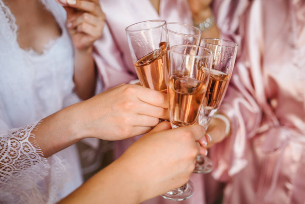 Young bridesmaids clinking with glasses of champagne in hotel room. Closeup photo of cheerful girls celebrating a bachelorette party. Females have toast with wine. - Foto, Imagen