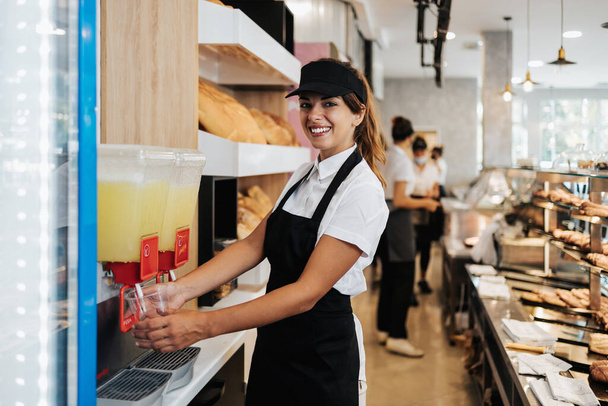 Beautiful young and happy female worker working in a modern bakery or fast food restaurant. - Fotografie, Obrázek