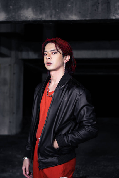 un uomo asiatico con i capelli rossi e una giacca nera posa in un edificio abbandonato di notte - Foto, immagini