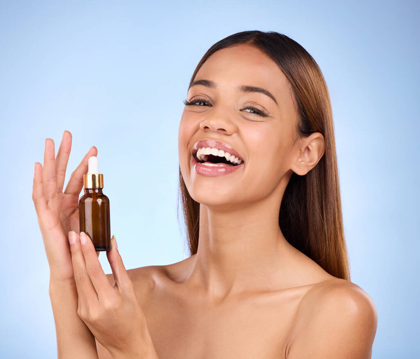 Beauty, skincare and hispanic woman holding serum with smile for anti aging skin glow on blue background. Cosmetics, facial repair and face of model with solution or collagen product in studio promo - 写真・画像