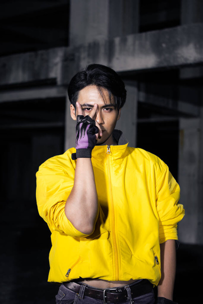 an asian man with a yellow jacket and black hair posing very gallantly in an abandoned building - Foto, afbeelding