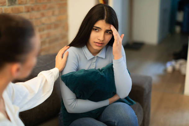 Unhappy teen lady having problem, hugging pillow and talking with friend who showing compassion and trying to appease. Friendly support in difficult time, comforting through emotional problems - Foto, Imagem