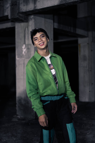 an Asian man smiles while wearing a green parachute jacket and black pants at night - Zdjęcie, obraz