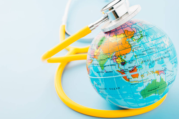 World Health Day. Top view yellow doctor stethoscope wrapped around world globe isolated on pastel blue background with copy space for text, Global healthcare, Health care and medical concept - Фото, изображение