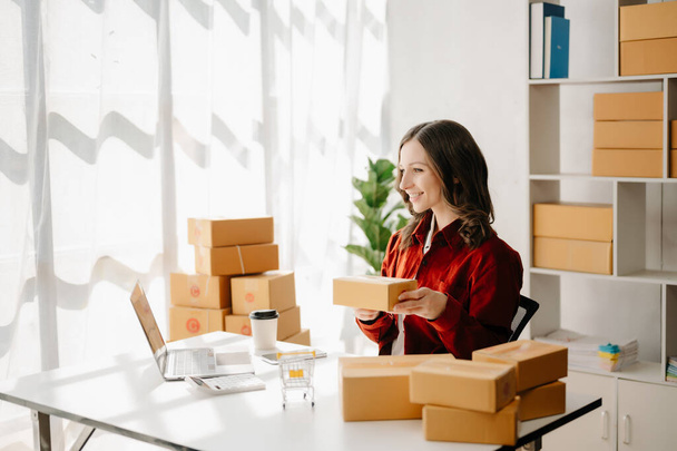 Startup small business SME, Entrepreneur owner woman using laptop taking receive and checking online purchase shopping order to prepare pack product boxes.  at home office - Foto, Bild