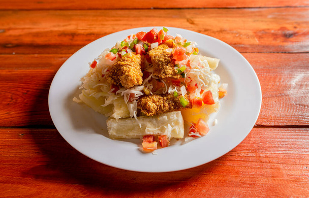 Traditional chicharron dish with cassava and tomato salad. Latin food chicharron con yuca served on wooden table. Nicaraguan dish chicharron with cassava on the table. - Photo, Image