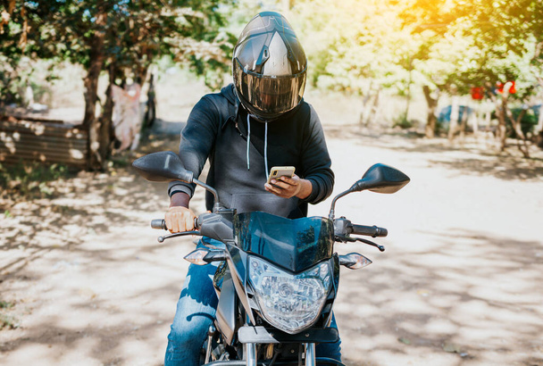 Egy motoros férfi sms-ezik vezetés közben. Motoros motoros, mobiltelefonnal a szabadban. Koncepciója zavart motoros mobiltelefonnal. - Fotó, kép