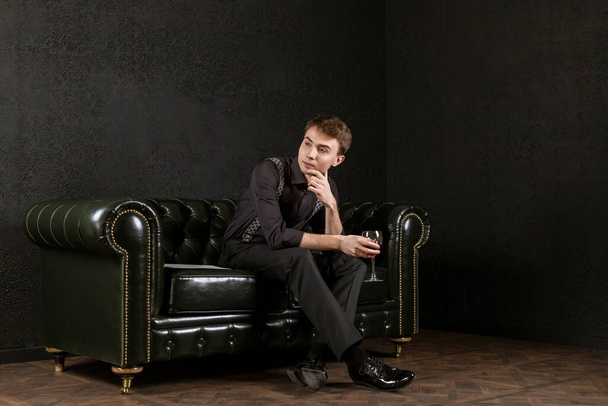 Genç bir adam elinde bir bardak şarap ve müzik kağıtlarıyla karanlık bir odada zarif bir kanepede oturmuş kompozisyon üzerinde kafa yoruyor. Yaratılış süreci. - Fotoğraf, Görsel