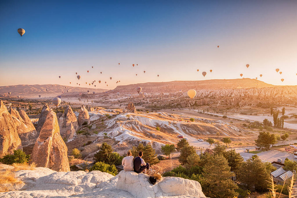 Φίλοι που κάθονται στην κορυφή του λόφου και θαυμάζουν τη θέα των μαγευτικών ιπτάμενων αερόστατων θερμού αέρα στην Καππαδοκία - Φωτογραφία, εικόνα
